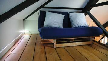 A loft-style bedroom with a wooden floor, a blue bed with patterned pillows, and a sloped ceiling.
