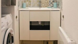 Une petite salle de bain équipée d’un lave-linge, d’un lavabo avec un miroir et de carreaux décorés.