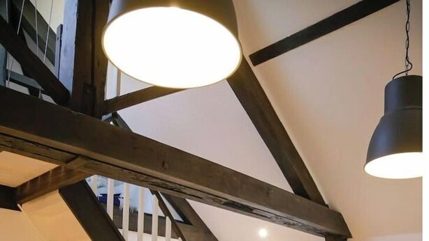 Une pièce de style « loft », avec des poutres en bois apparentes, un escalier, une table à manger et un canapé.