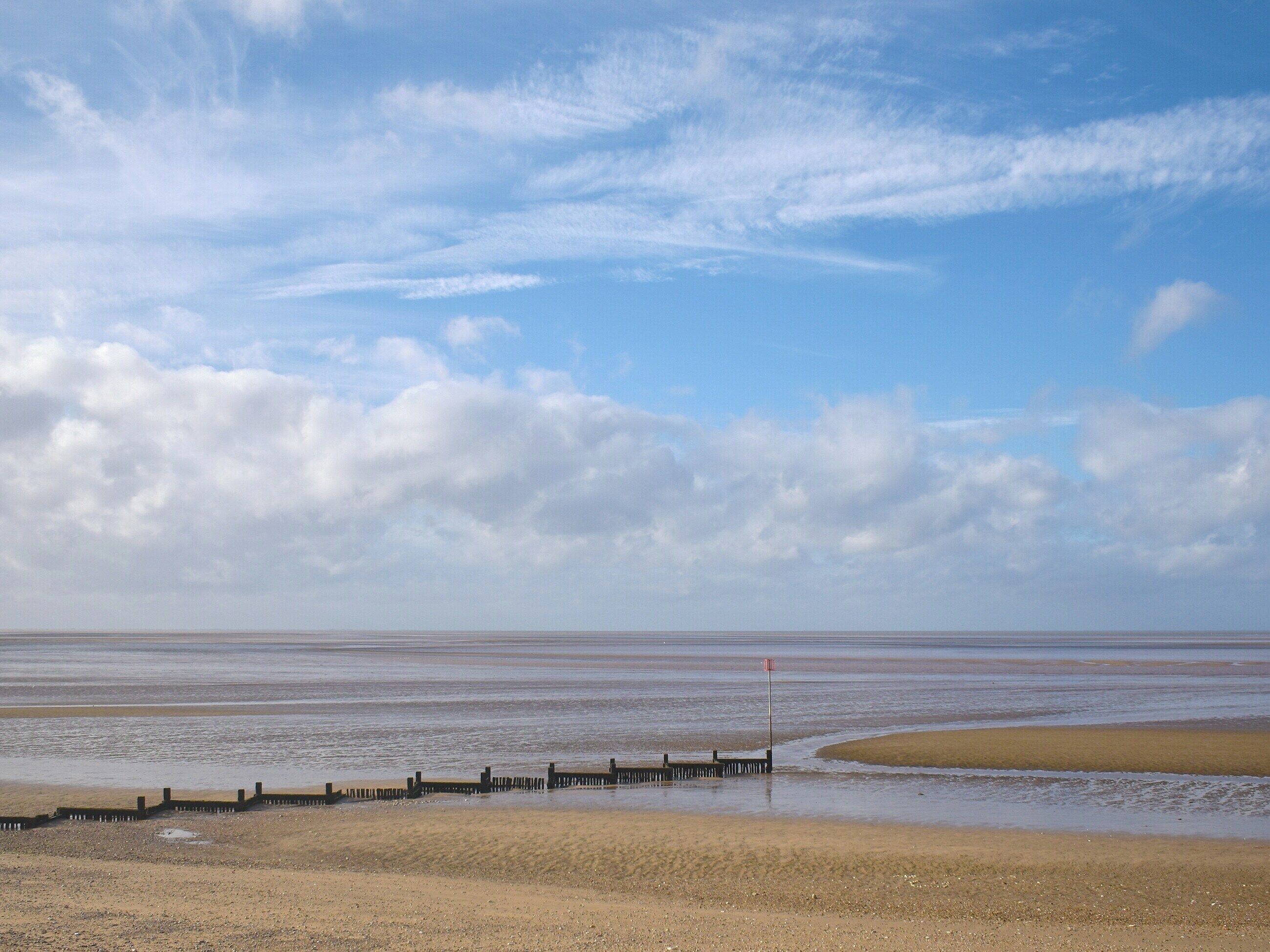 Un paysage côtier avec une plage de sable, une jetée en bois et un drapeau rouge servant de balise.