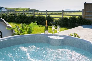 A hot tub with a bottle of champagne and two glasses, surrounded by a lush garden and a wooden fence. - Cysgod y Llanw -  an on the beach that sleeps 6 guests  in 3 bedrooms (Llanfaethlu)