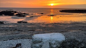 Ein Küsten-Sonnenuntergang mit felsigem Vordergrund und ruhiger See.