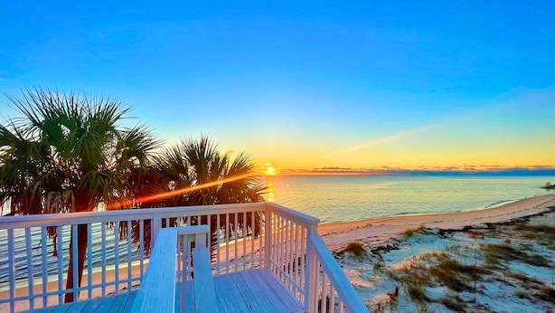 A wooden deck with a railing overlooking a beach at sunset.