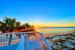 Un terrazzo in legno con ringhiera che si affaccia su una spiaggia al tramonto.