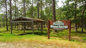 A wooden sign for Panacea Mineral Springs with a picnic shelter in the background.