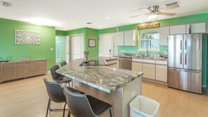 A modern kitchen with green walls, a marble island, stainless steel appliances, and a ceiling fan.