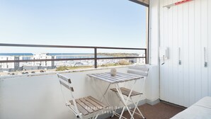 A balcony with a view of the marina and buildings, a white folding chair, and a small table with a vase. - Vacation apartment Meerblickbude (Wendtorf)