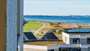 A view of a coastal area with a golf course, a body of water, and buildings in the foreground. - Vacation apartment Meerblickbude (Wendtorf)