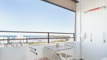 Een balkon met uitzicht op de jachthaven en gebouwen, een witte klapstoel en een tafeltje met een vaas.