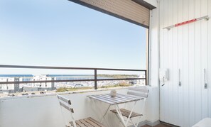A balcony with a view of the marina and buildings, a white folding chair, and a small table with a vase.