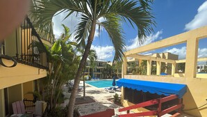 A pool area with a blue canopy, palm trees, and a red railing. - Air-conditioned 1 bed 1 full bath 1 half bath apartment.  Hot Water & generator. (Sosúa)