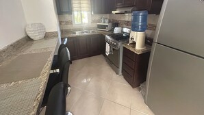 A kitchen with dark wooden cabinets, a stainless steel stove, a sink, and a refrigerator. - Air-conditioned 1 bed 1 full bath 1 half bath apartment.  Hot Water & generator. (Sosúa)