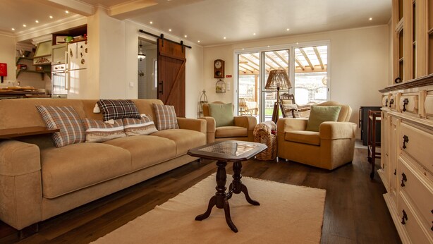 A spacious living room with a beige sofa, a coffee table, and a fireplace. - Casa da Porta Amarela - Holiday Home in the Seven Cities (Ponta Delgada)