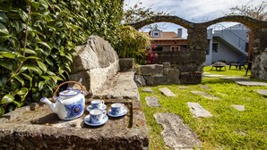 A stone bench with a teapot and cups, surrounded by greenery and a stone wall. - Casa da Porta Amarela - Holiday Home in the Seven Cities (Ponta Delgada)