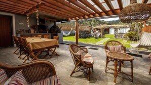 An outdoor patio with a dining table, wicker chairs, and a hanging light fixture. - Casa da Porta Amarela - Holiday Home in the Seven Cities (Ponta Delgada)
