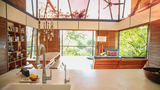 Una cocina moderna con un ventanal amplio, estanterías de madera y un comedor con vistas a zonas verdes.