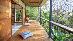 Una terraza de madera con techo de bambú, dos sillones de descanso y vistas a exuberante follaje.