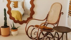 A room with a rocking chair, a small round table, and two potted plants. - Luxe Desert Retreat: Hot Tub, Cowboy Pool & Outdoor Shower (Yucca Valley)