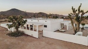 A modern white building with a flat roof, surrounded by desert landscape and mountains. - Luxe Desert Retreat: Hot Tub, Cowboy Pool & Outdoor Shower (Yucca Valley)