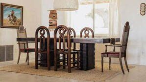 A dining area with a wooden table and chairs, a large pendant light, and a painting on the wall. - Luxe Desert Retreat: Hot Tub, Cowboy Pool & Outdoor Shower (Yucca Valley)
