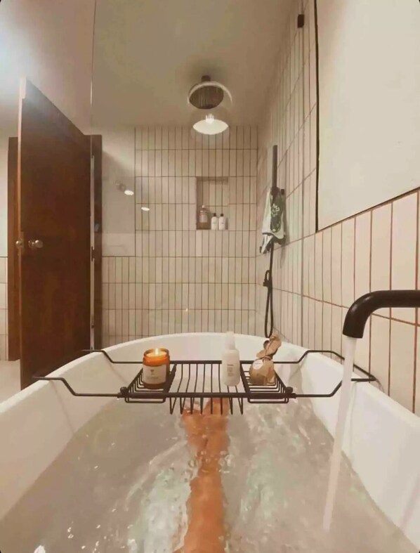 Una bañera con un estante que contiene artículos de aseo, un cabezal de ducha y un perchero para toallas.