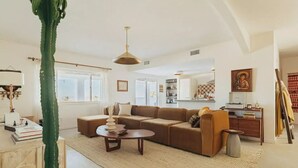 A living room with a large sectional sofa, a coffee table, and a hanging light fixture. - Luxe Desert Retreat: Hot Tub, Cowboy Pool & Outdoor Shower (Yucca Valley)