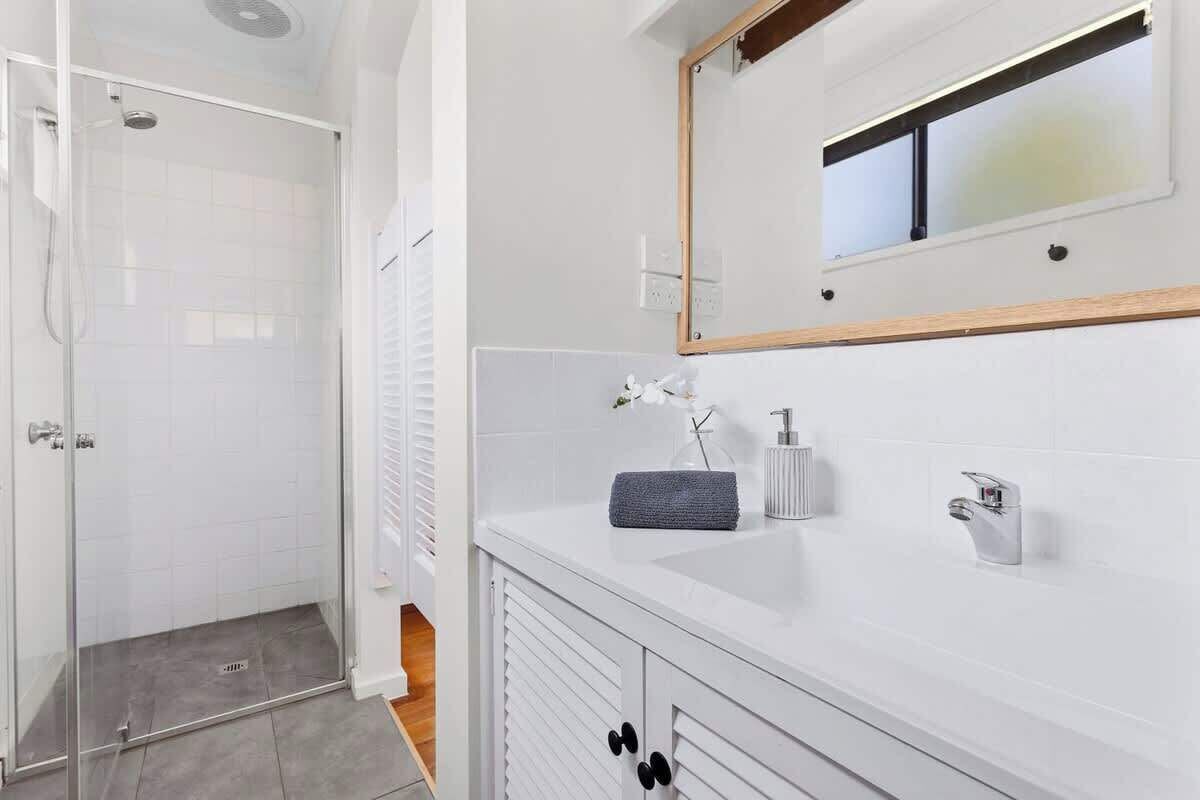 A modern bathroom with a glass shower enclosure, a white vanity with a mirror, and a towel on the counter.