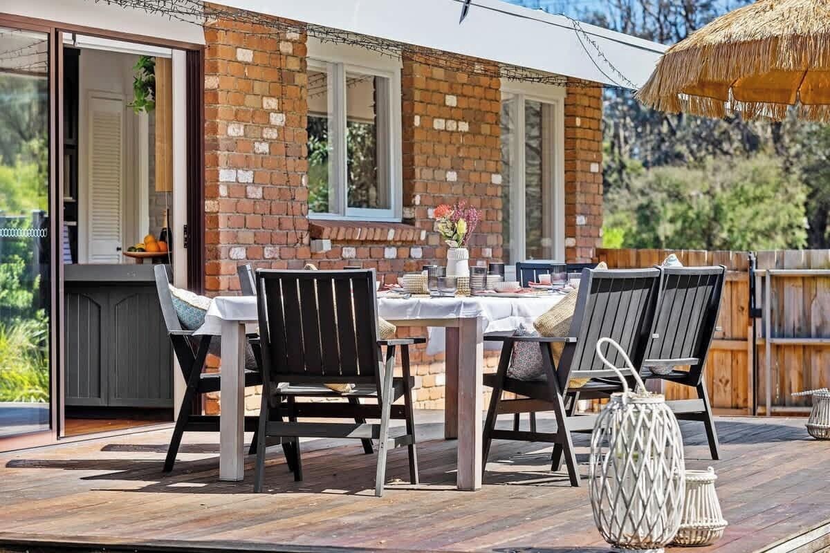 An outdoor patio with a brick wall, a table set for dining, and two chairs.