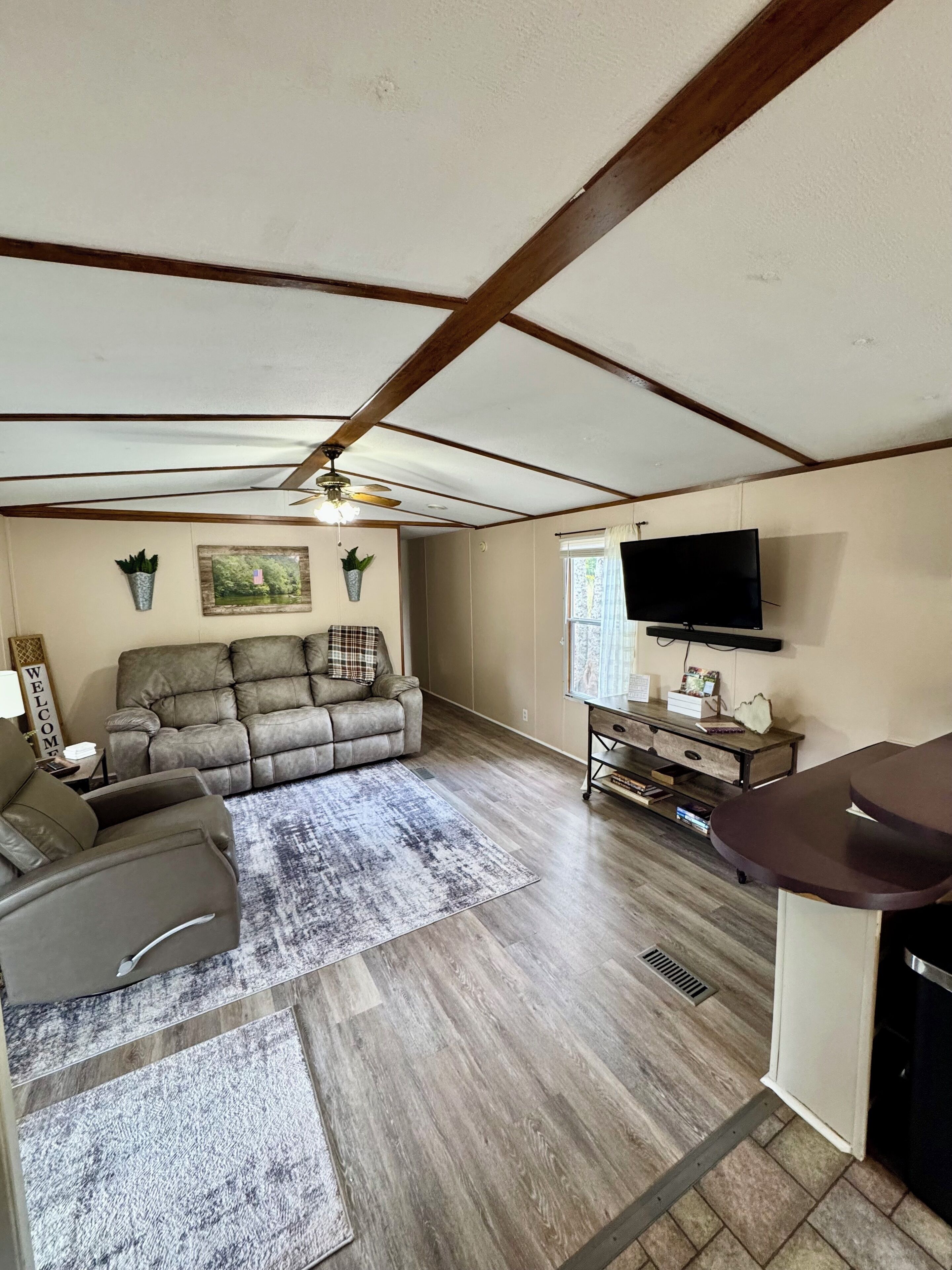 A spacious living room with a sectional sofa, a flat-screen TV, and a ceiling fan.