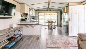 A compact kitchen with a dining area, a TV mounted on the wall, and a small seating area with a couch. - Dorothy’s Retreat (Campbellsville)