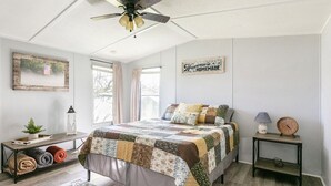 A bedroom with a bed, a nightstand, a lamp, a clock, a framed picture, and a window. - Dorothy’s Retreat (Campbellsville)