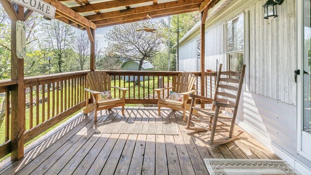 A wooden porch with a 'WELCOME' sign, outdoor seating, and a view of the surrounding greenery. - Dorothy’s Retreat (Campbellsville)