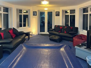 A room with a blue padded area, black leather sofas with red cushions, a white desk, and a door leading to another room.