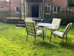 A patio with a round table and four chairs, a brick building in the background, and a wooden deck. - 2 bedroom accommodation in Blaydon Burn, near Newcastle upon Tyne (Blaydon Burn, near Newcastle upon Tyne)