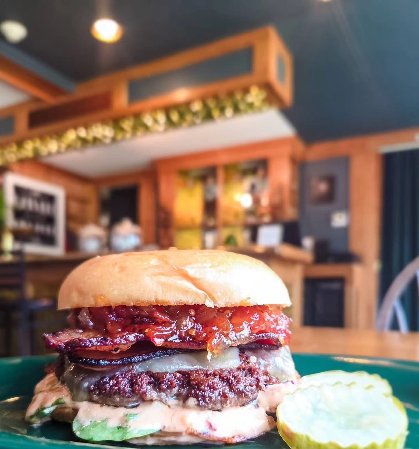 Una hamburguesa con tocino, lechuga y pepinillo sobre un plato verde.