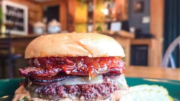 Una hamburguesa con tocino, lechuga y pepinillo sobre un plato verde.