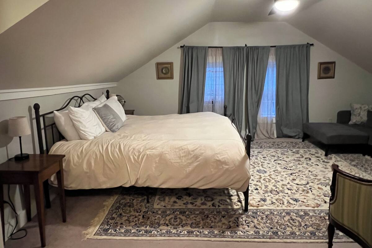A bedroom with a bed, a desk, a chair, a ceiling fan, and a patterned rug.