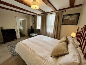 A bedroom with a large bed, a chair, a desk, and a window with curtains. - Independence Inn (Strafford)