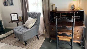 A room with a grey armchair, a wooden dresser, a green desk lamp, and a framed certificate on a small table.