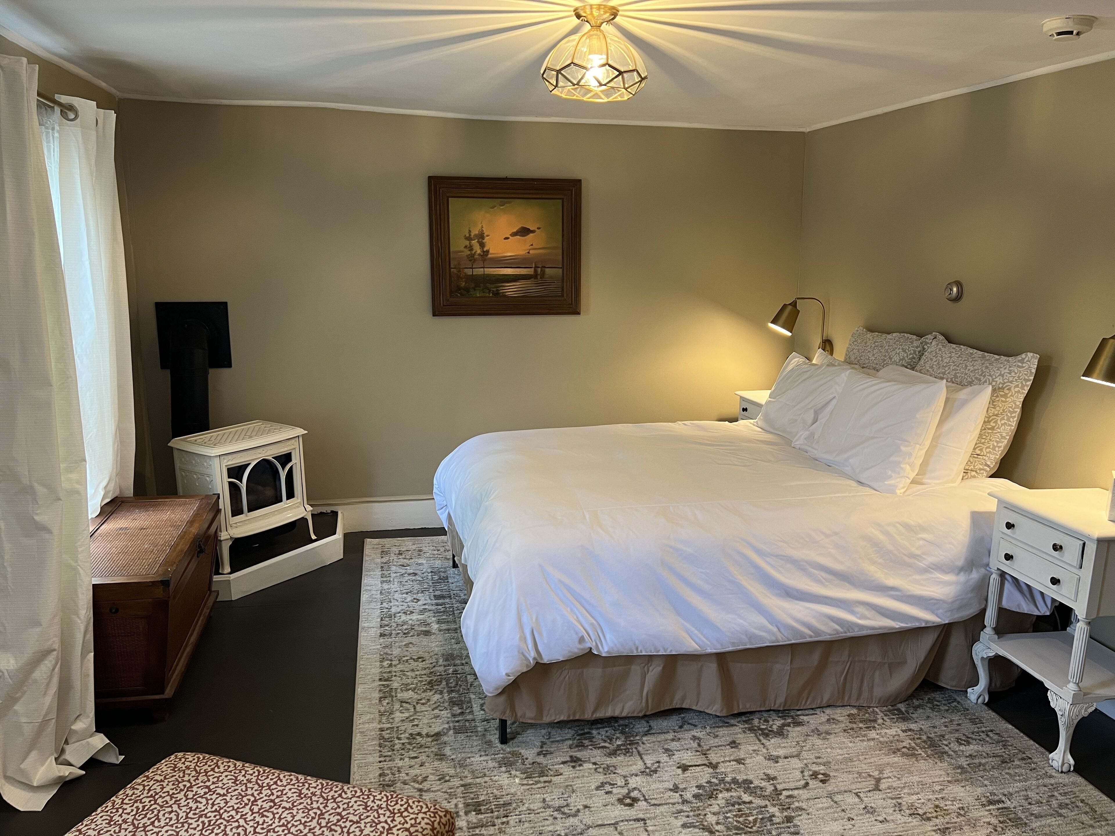 Une chambre à coucher avec un grand lit, des tables de chevet, une commode, une lampe, un tableau au mur et un luminaire au plafond.