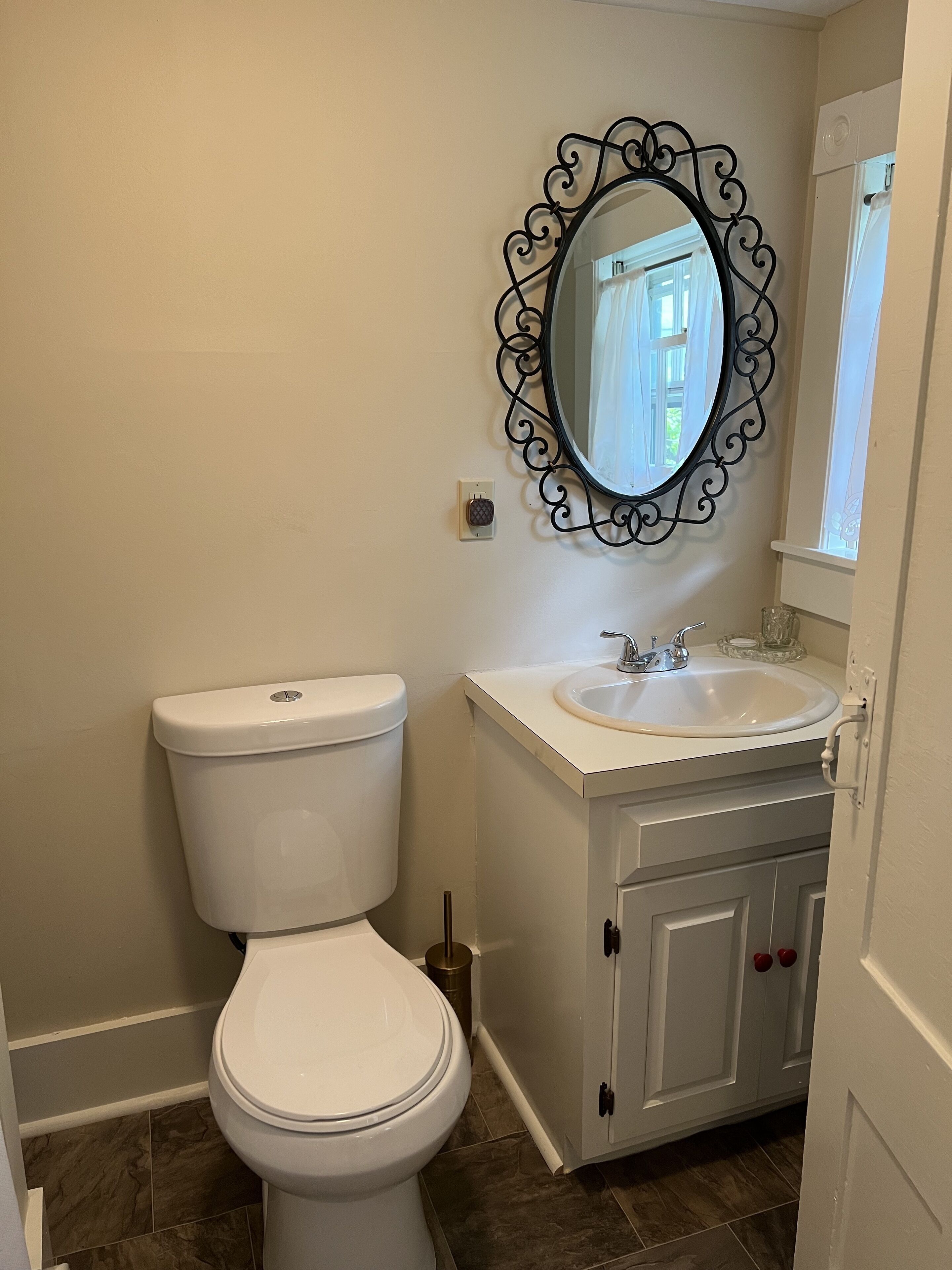 Un baño con inodoro blanco, lavabo con espejo arriba y un mueble con pomos rojos.
