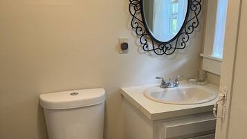 Un baño con inodoro blanco, lavabo con espejo arriba y un mueble con pomos rojos.