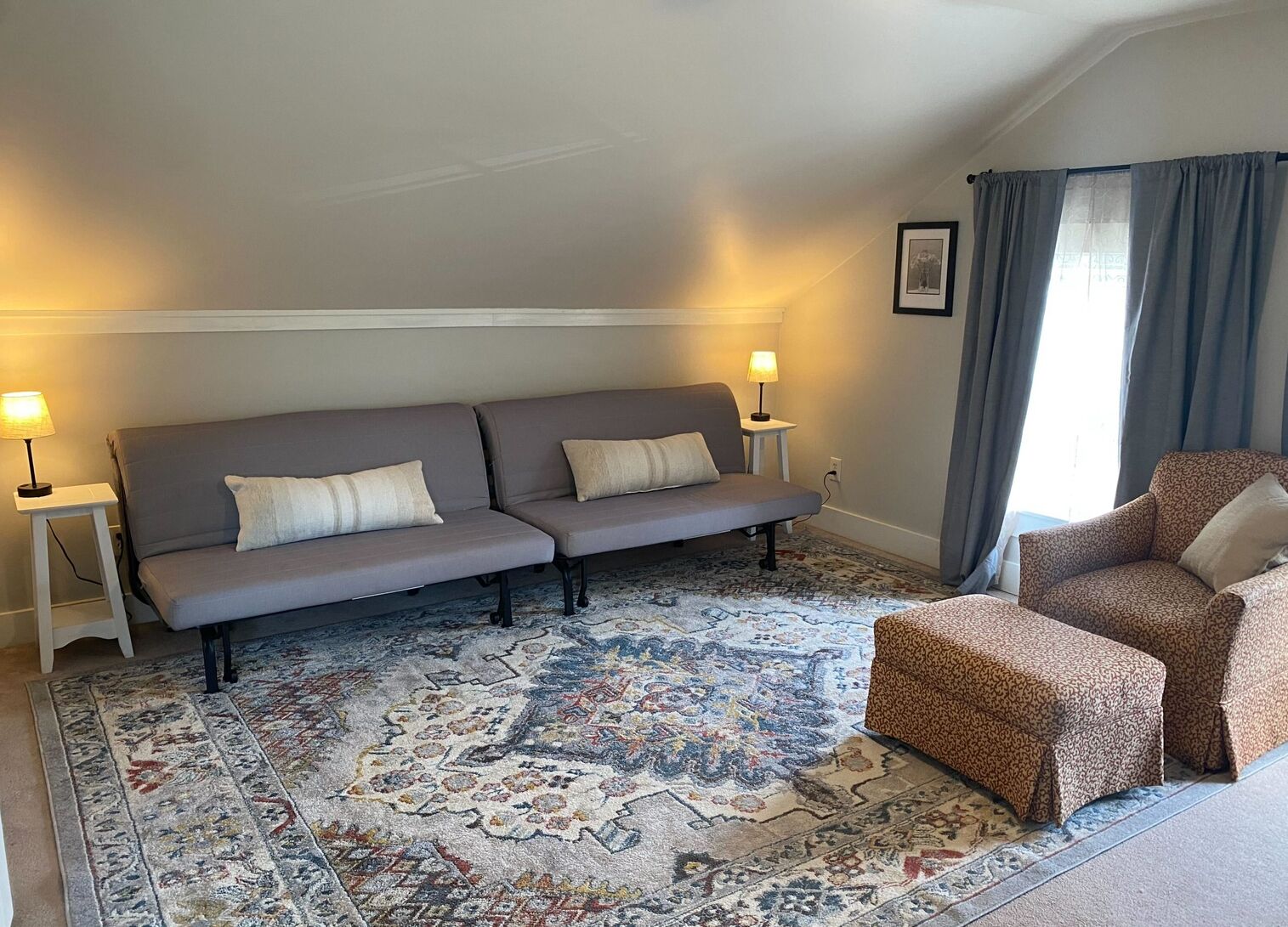 A room with a grey sofa, two side tables with lamps, a patterned rug, and a leopard print chair.