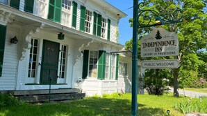 A white building with green shutters, a sign for Independence Inn, and a grassy area in front. - Independence Inn (Strafford)
