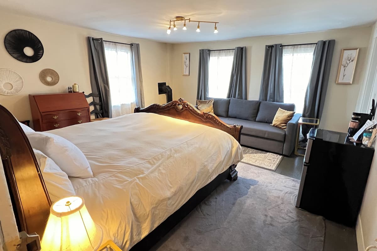 A bedroom with a large bed, a sofa, a desk, and a lamp.