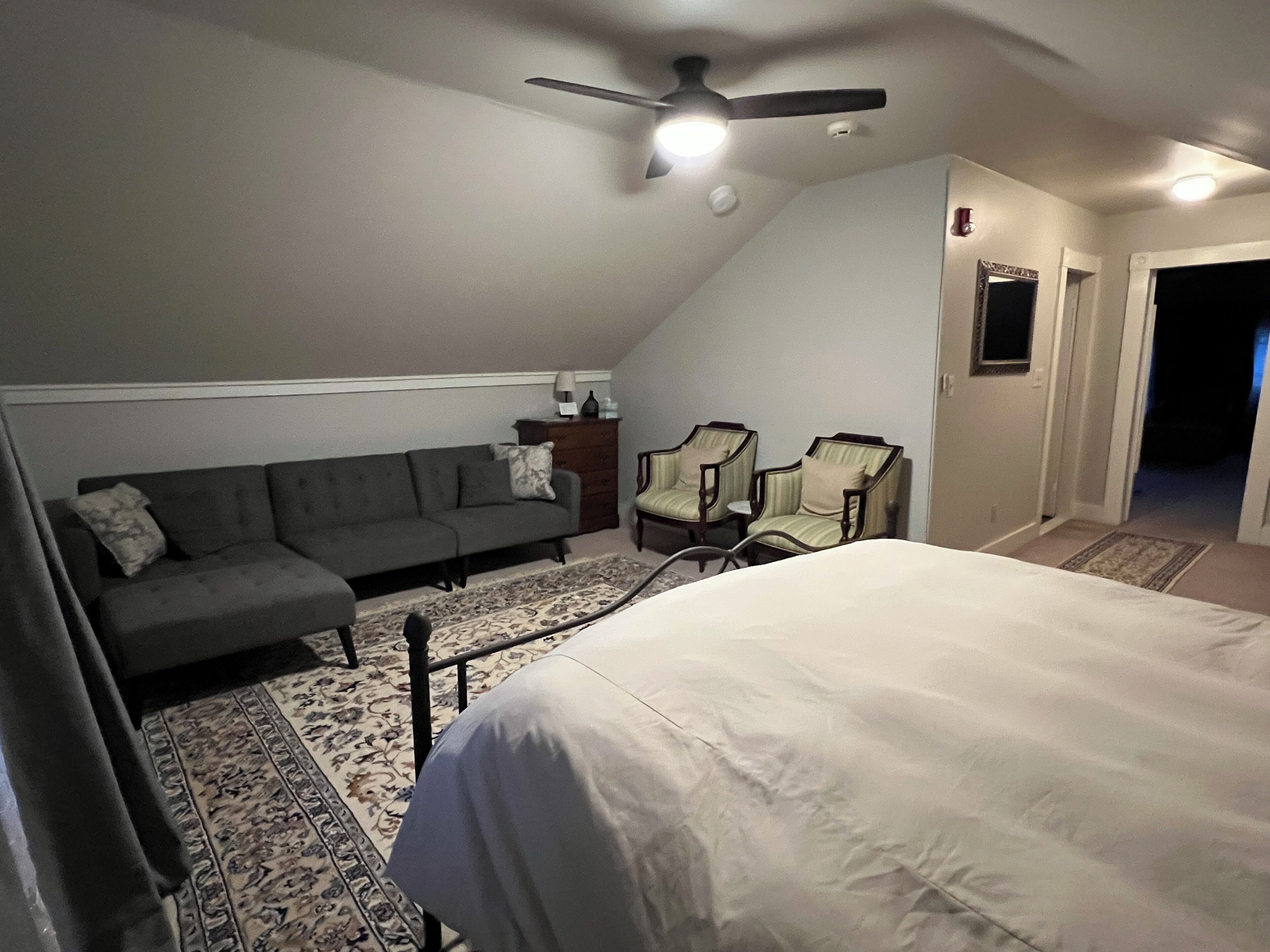 Une chambre à coucher comprenant un lit, un canapé, deux fauteuils, un ventilateur de plafond et une table de chevet.