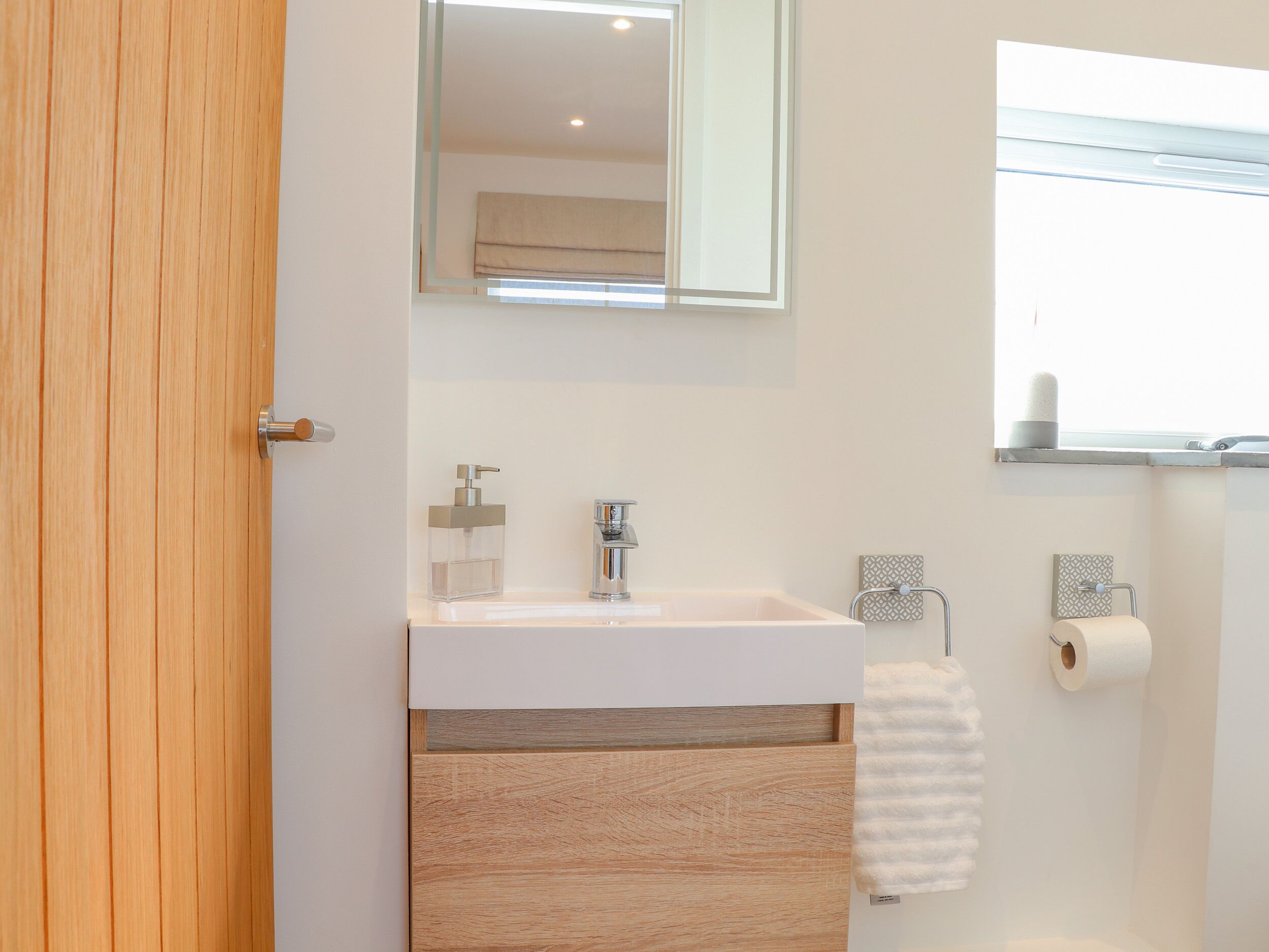 A bathroom with a wooden door, a white sink with a mirror above it, a towel rack, and a toilet paper holder.