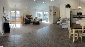 Uma sala de estar espaçosa com lareira, área de jantar com uma mesa grande e cadeiras, e cozinha com armários brancos e eletrodomésticos modernos.