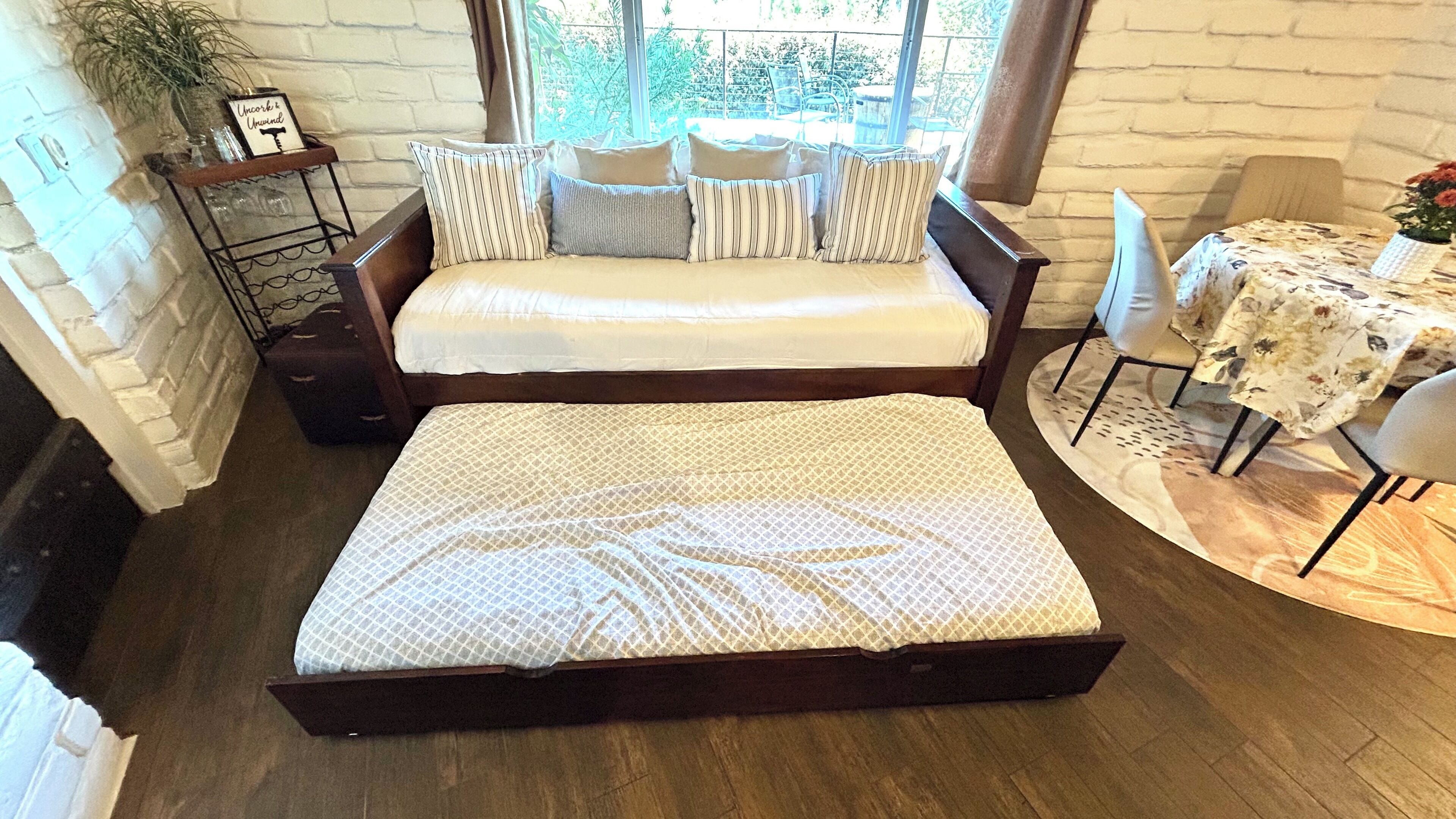 A cozy room with a bed, a small table with a floral tablecloth, and a view of the outdoors.