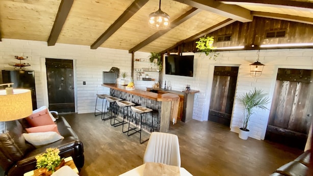 A cozy living area with a black leather sofa, a wooden bar with stools, and a white brick wall. - Tranquil country setting w/majestic views (Escondido)